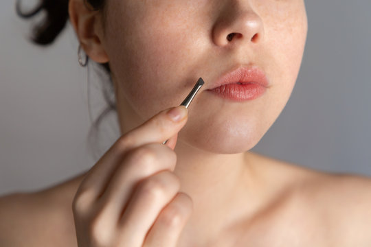 A young woman holds tweezers over her upper lip. The concept of getting rid of unwanted facial hair