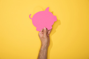 cropped view of man holding paper icon of pink piggy bank on yellow