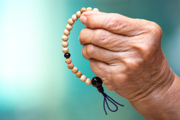 Senior woman's hands praying and holding a beads rosary in bokeh blue swimming pool background, Asian Body language feeling, Prayer buddhist, Religious concept