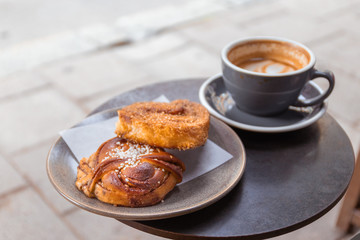 Cup of coffee and bun with cinnamon lying on the table in cafe