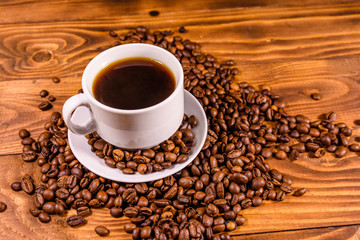 Cup of hot coffee and scattered coffee beans on wooden table