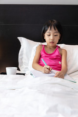 Asian Little Chinese Girl doing homework in bed