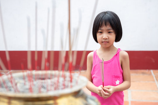 Asian Little Chinese Girl praying with burning incense sticks