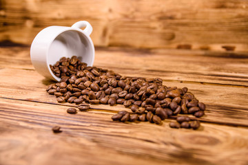 White cup and scattered coffee beans on wooden table