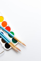 Top view of paintbrushes palette and watercolor paints with white space
