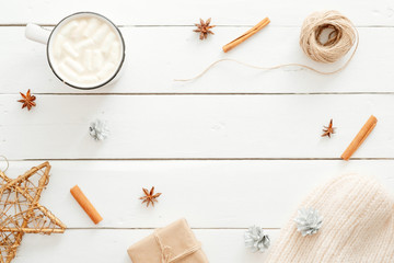 Christmas minimal composition. Flatlay cup of hot chocolate with marshmallow, cinnamon sticks, Xmas decorations, gift box wrapped kraft paper, knitted scarf on wooden white background. Hygge Christmas