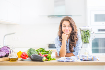 Woman making vegetable soup or smoothies with blender in her kitchen. Young happy woman preparing healthy drink with spinach broccoli arugula and other vegetable.