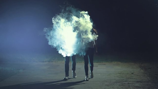 The man and woman walking in the night park near the smoke cloud. slow motion