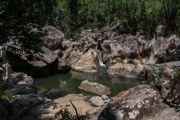 Naklejka na ściany i meble A small waterfall and wild pool in the mountains of Vietnam. Rocks and water, green bushes and trees