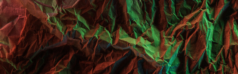 top view of glossy crumpled foil with colorful lighting reflection in darkness isolated on black