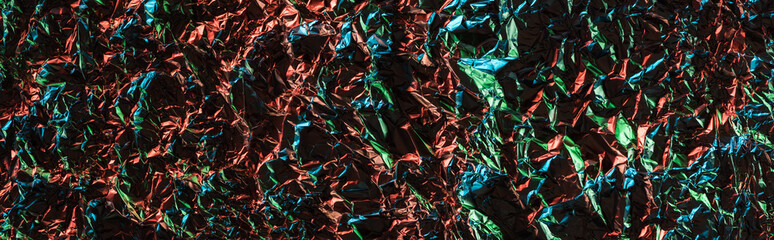 top view of glossy crumpled foil with colorful lighting reflection in darkness isolated on black