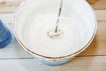 Man is mixing spackling glue in the bucket. Wallpaper hanging in the flat. Restoration indoors. Renovation works.
