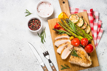 Chicken breast grilled with vegetables on a wooden serving board.