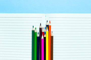 Back to school concept. Color pencils and clean notebook in line on blue background top view flat...