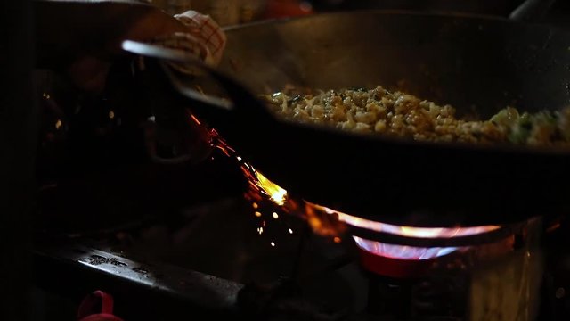Awesome slow motion shot of a street vendor cooking their Indonesian food. The food is cooking in a pot over a flame stove. The meal is fried rice (Nasi Goreng) with egg, onions, and various spices.