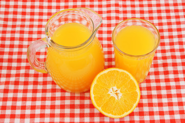 Orange juice in glass and pitcher on red tablecloth
