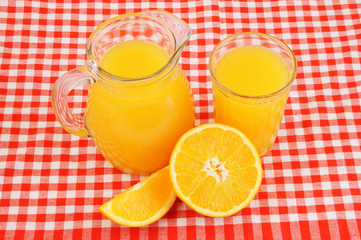 Fresh orange juice in glass and jar with orange fruit on red tablecloth