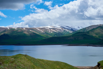 view of a mountain lake against the backdrop of a mountain with snow-capped peaks on a sunny day with clouds in the sky.