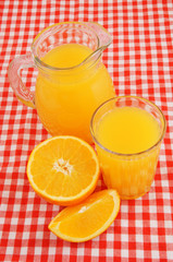 Fresh orange juice in glass and jar with orange fruit on red tablecloth