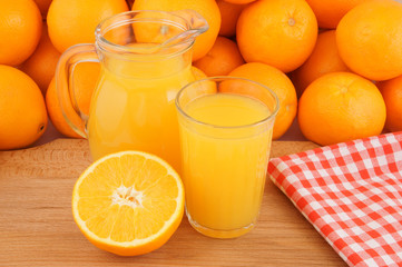 Fresh orange juice on wooden table with many oranges as background
