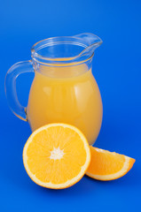 Orange juice in pitcher with orange fruit slices on blue background