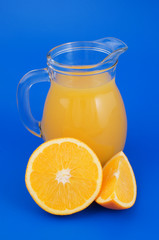 Orange juice in pitcher with orange fruit on blue background