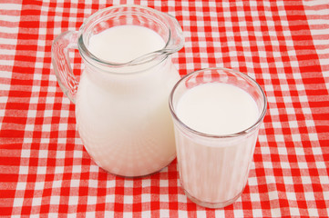 Milk in pitcher and glass on red tablecloth 