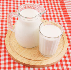 Milk in jar and glass with wooden board on tablecloth