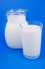 Glass and jar with milk on blue background