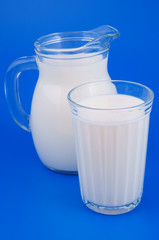 Glass and pitcher with fresh milk on blue background 