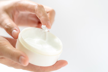 Female hands holding and apply jar of nourishing cream  on white background.Skin care and beauty concept.Closeup.