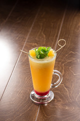 Winter hot drink from oranges and berries in tall glass on wooden table