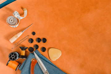 Orange textured background with sewing tools, copy space on natural leather on background. Frame...