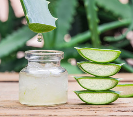 Fresh aloe leaves and aloe gel in the cosmetic jar on wooden table.