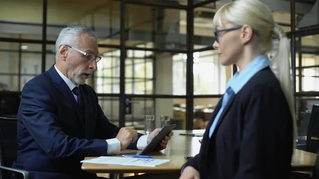 Senior boss praising female employee shaking hand, using business tablet app