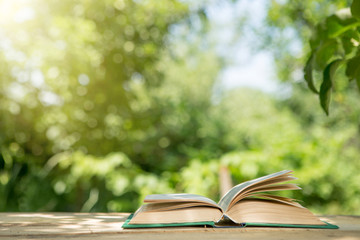 Studying in summer concept. Open book on a wooden table in a garden, sunny summer day