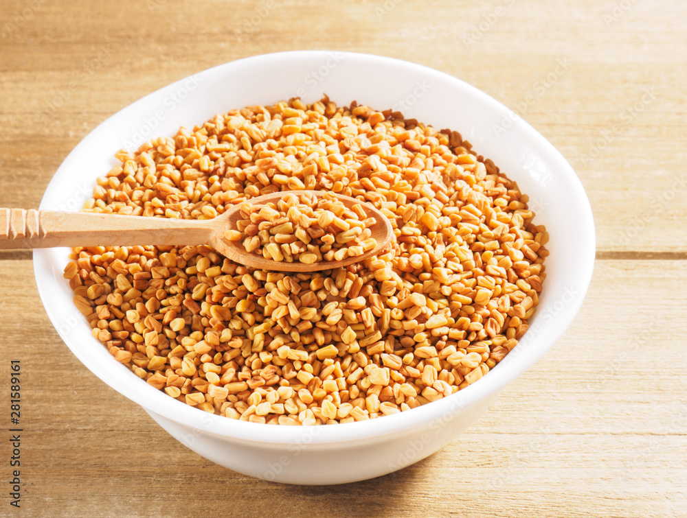 Wall mural fenugreek (trigonella) in a ceramic white cup with spoon on a wooden background