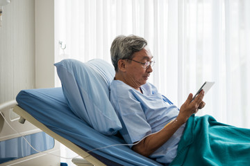 Happy elderly patient sitting on bed and making video call with tablet at hospital.