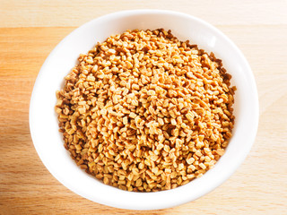 Fenugreek (Trigonella) in white ceramic cup on a wooden background