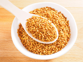Fenugreek (Trigonella) in white cup on a wooden spoon on a wooden background