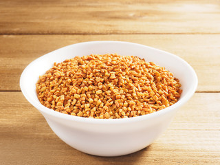 Fenugreek (Trigonella) in a white ceramic cup on a wooden background