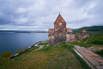 Fototapeta na wymiar The ancient monastery is located on top of the endless water expanses of the Lake Sevan on an overcast day with clouds in the sky.