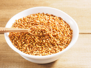 Fenugreek (Trigonella) in a ceramic white cup with spoon on a wooden background