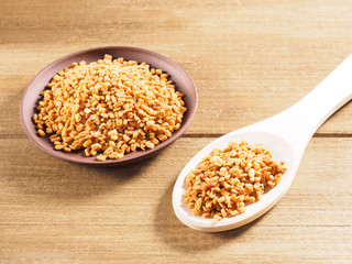 Fenugreek (Trigonella) in a clay plate with spoon on a wooden background