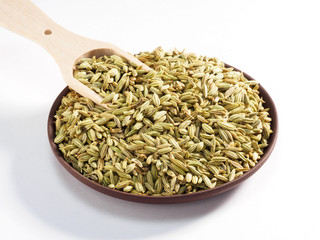 Fennel seeds (Foeniculum vulgare) in a clay plate with scoop on a white background