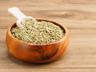 Fennel seeds (Foeniculum vulgare) in a wooden brown cup with scoop on a wooden background