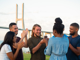 Cheerful people giving cake to smiling friend and applauding. African American woman presenting...