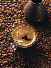 Glass Cup of espresso coffee stands on coffee beans close-up