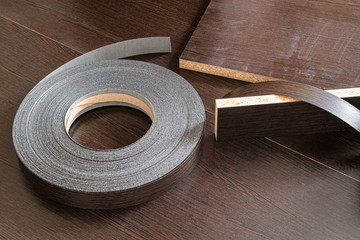Roll melamine edge for finishing of furniture. Edging tape lying on laminated chipboard sheets wenge color.