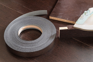 Roll melamine edge for finishing of furniture and smoothing-iron used for gluing edges. Edging tape on laminated chipboard sheets wenge color.